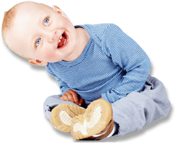 Ein fröhliches Baby sitzt schräg auf dem Boden, trägt ein blau gestreiftes Oberteil und lächelt breit in die Kamera.