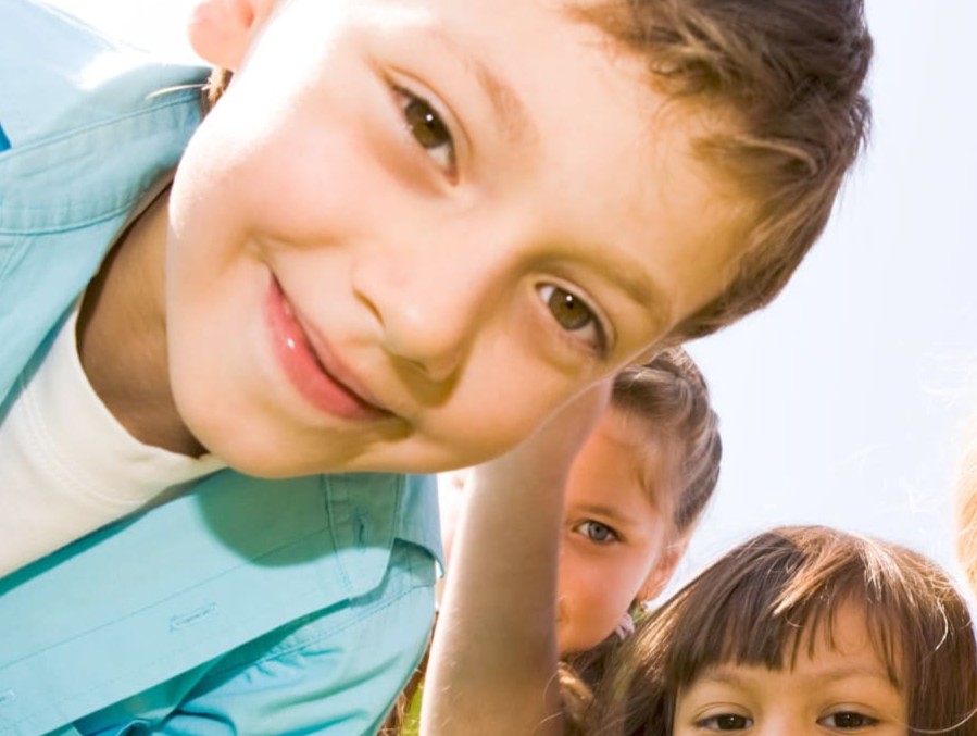 Mehrere Kinder beugen sich lachend zur Kamera, ein Junge im Vordergrund schaut neugierig in die Linse.