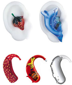 Mehrere bunte, kindgerecht gestaltete Hörgeräte und Ohrpassstücke in verschiedenen Designs, darunter Erdbeere, Delfin und Comicmotiv.